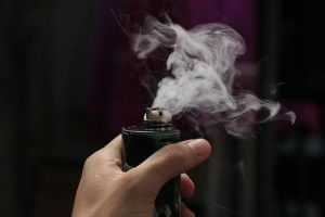Hand holding vaping device emitting vapor