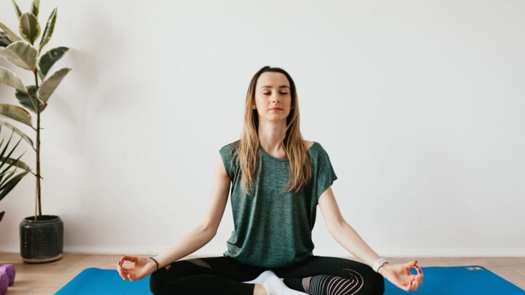 Woman sitting upright on a yoga mat with eyes closed, in the posture used for the Control Pause breathing test