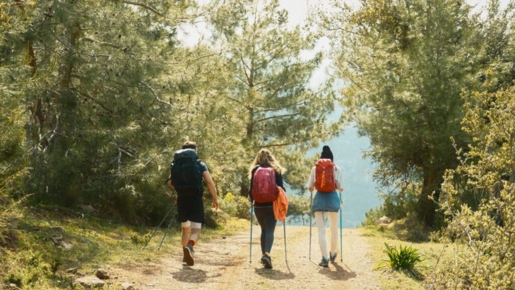 Three hikers with backpacks and trekking poles walking a sunlit trail on the Lycian Way, Turkey