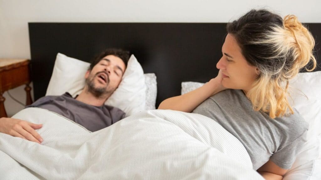 Woman lying awake looking at a man snoring beside her in bed
