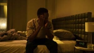 Man sitting awake at night on the edge of a bed with his head in his hands