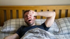 Man yawning and rubbing his forehead in bed after a poor night of sleep