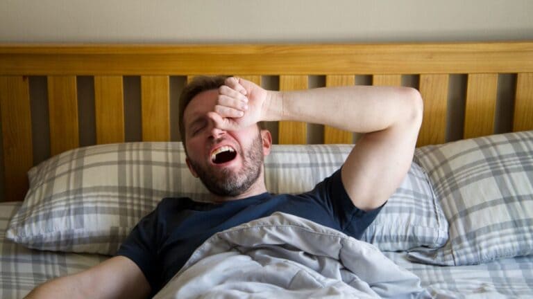 Man yawning and rubbing his forehead in bed after a poor night of sleep