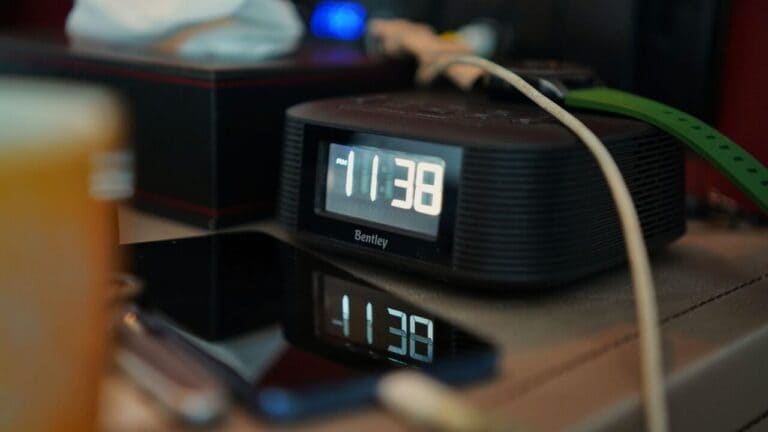 Smartphone charging on a nightstand next to a digital alarm clock reading 11:38