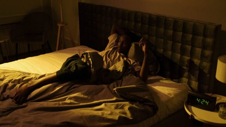 Man lying awake in a dimly lit bedroom with a clock beside the bed