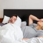 Couple in bed with one partner covering their face while the other sleeps