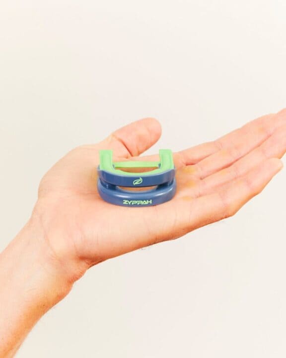 Zyppah anti-snoring mouthpiece resting in an open hand, showing its blue trays and green strap