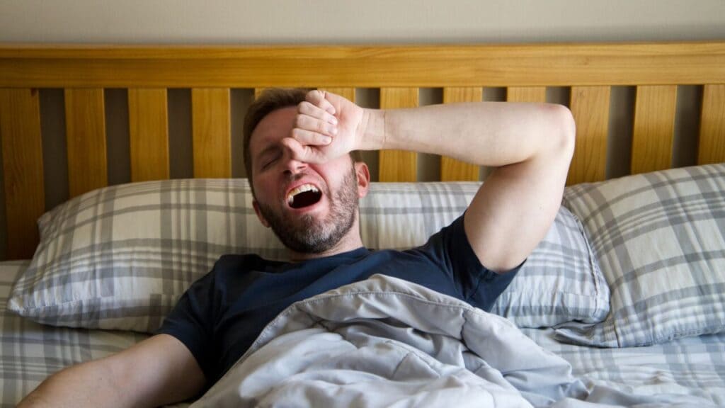 Man yawning and rubbing his forehead while lying in bed in the morning