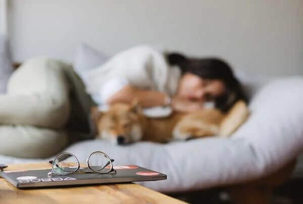woman sleeping on bed snuggled next to their dog. Adequate sleep is essential for daily function.