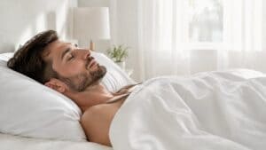 Man sleeping peacefully on his back in a bright bedroom with white bedding