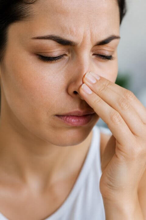 Close-up of a person touching their nose, appearing to experience nasal discomfort.
