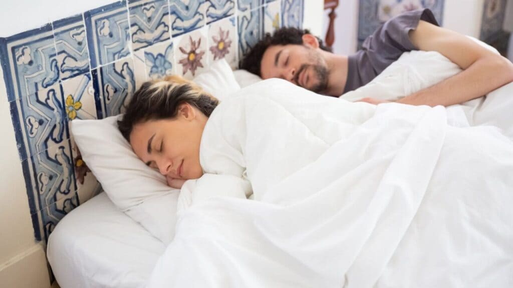 Couple sleeping peacefully side by side under a white duvet in a tiled bedroom