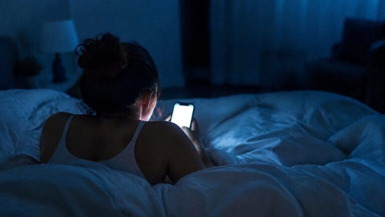 Woman lying in a dark bedroom looking at a bright phone screen